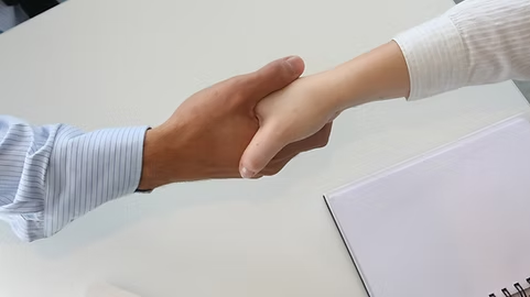 Two people shaking hands across a desk